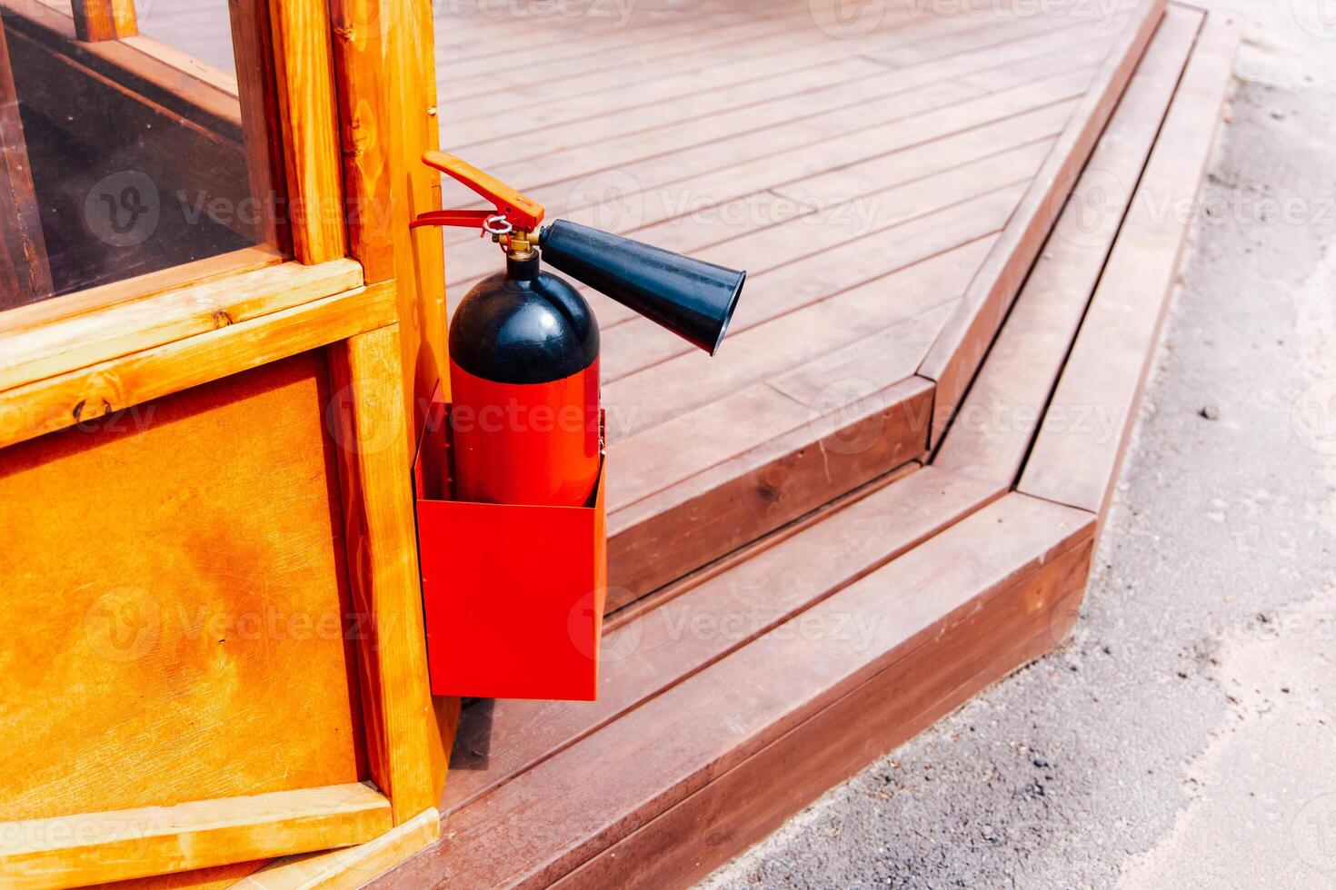 Fire extinguisher mounted outside a wooden structure near a deck area in bright daylight photo