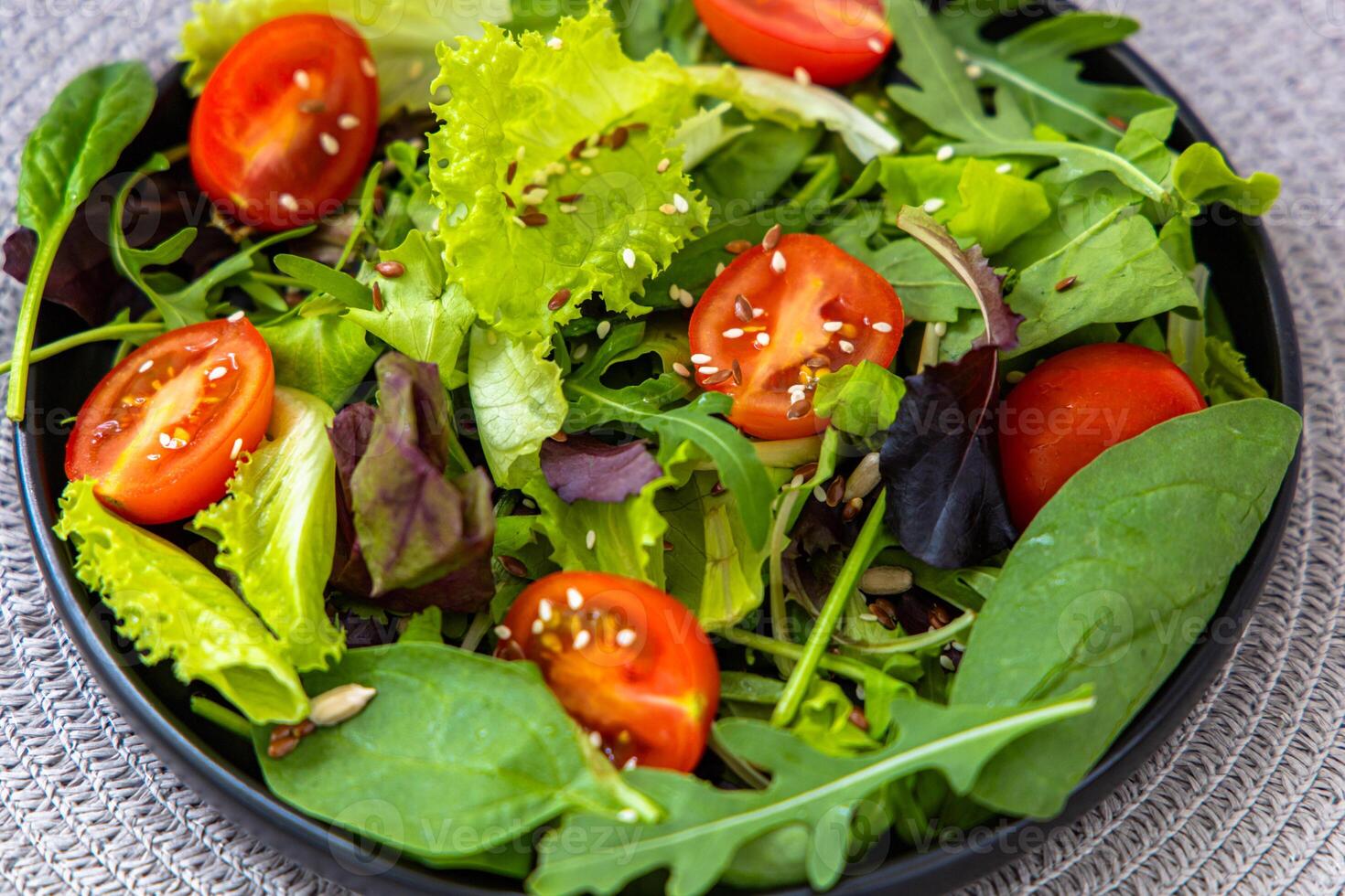 Fresh garden salad with assorted greens and cherry tomatoes in a black bowl photo