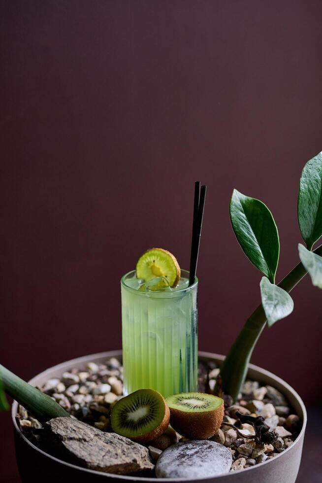 Kiwi juice in a glass with a straw and a kiwi on a wooden background photo