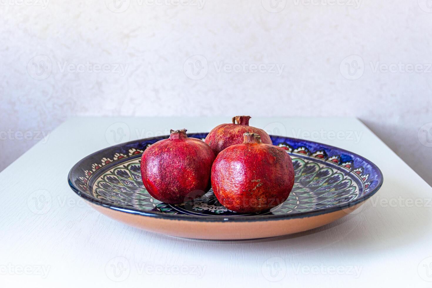 Three ripe pomegranates on a colorful handmade plate. Vibrant still life with rich textures and traditional ethnic design. photo