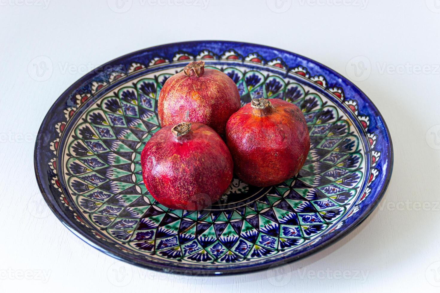 Three ripe pomegranates on a colorful handmade Uzbek ceramic plate. Vibrant still life with textures and traditional ethnic design. photo