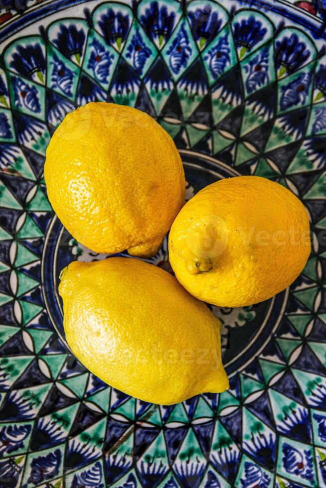 Bright yellow lemons on a patterned blue plate, showcasing vibrant color contrast and detailed citrus textures. photo