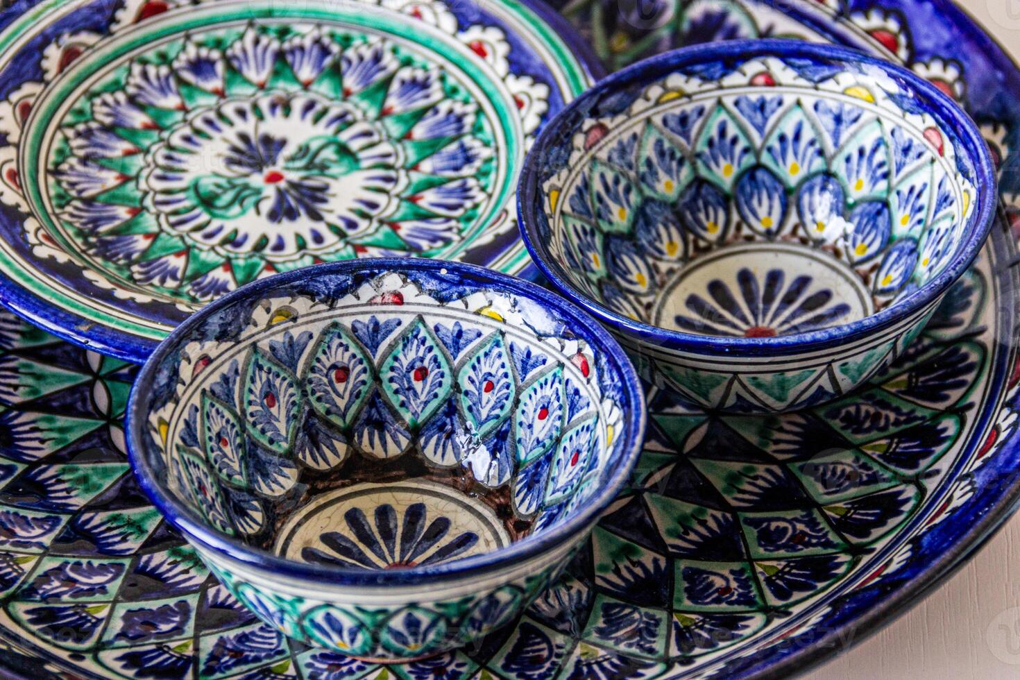 Ceramic dishes with intricate oriental patterns feature vibrant blues, greens, and whites. The design includes geometric shapes and floral motifs, with a high gloss finish. photo