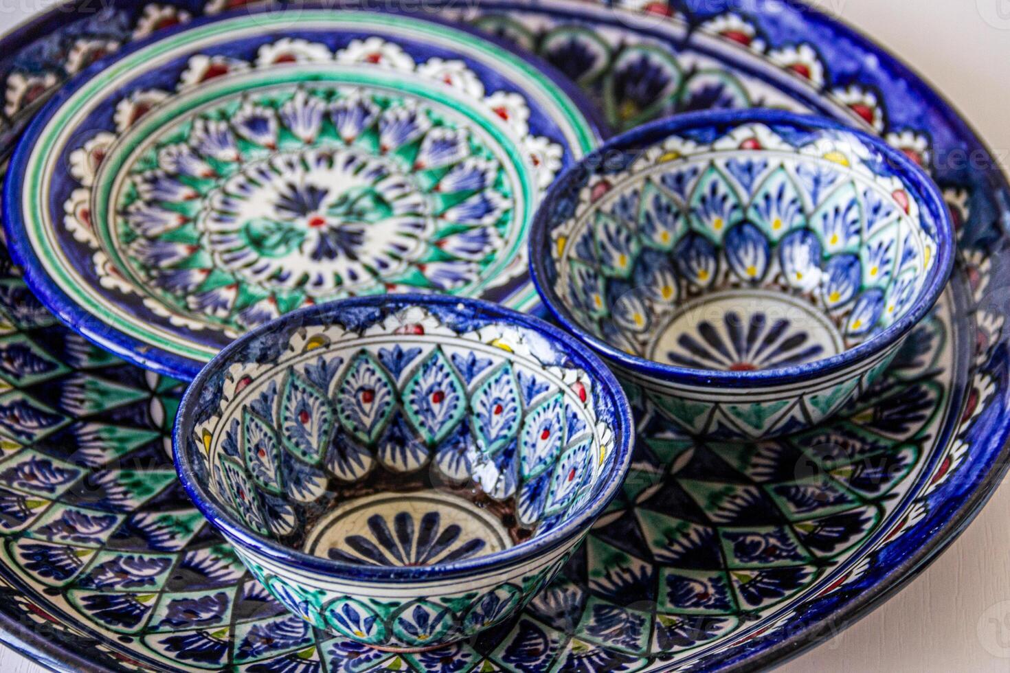 Ceramic dishes with intricate oriental patterns feature vibrant blues, greens, and whites. The design includes geometric shapes and floral motifs photo