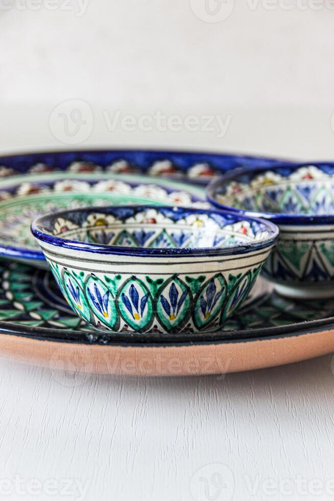A collection of traditional Uzbek ceramic dishes, showcasing intricate oriental patterns. The dishes feature a harmonious blend of blues, greens, and yellows with geometric and floral motifs. photo