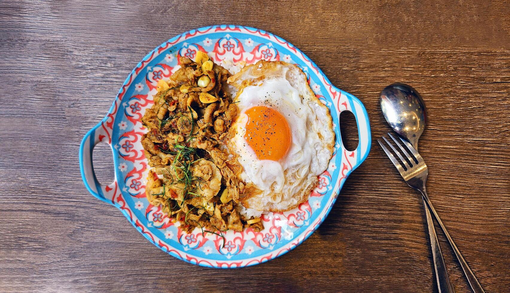 Top view of Stir fried beef, pork or chicken with southern yellow curry paste over rice with Thai fried egg and spoon with fork on wooden background. photo