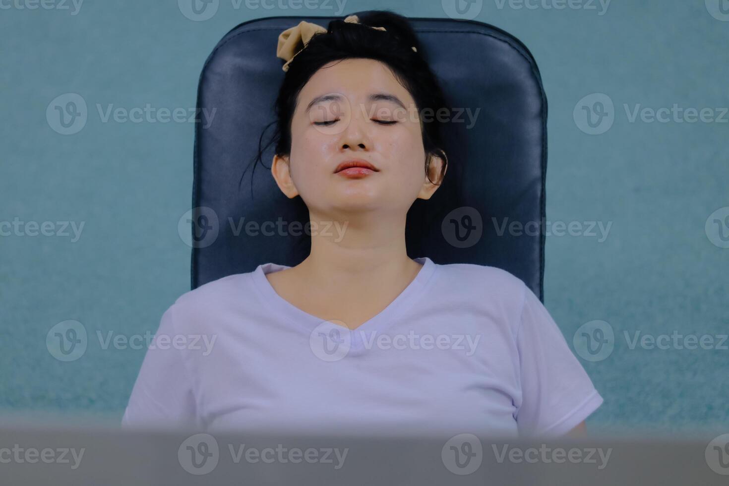 woman sitting in a dark chair. Her eyes are closed and her head is leaning on the back of the chair. giving the impression of relaxation and calm. indicating a moment of peaceful rest or contemplation photo