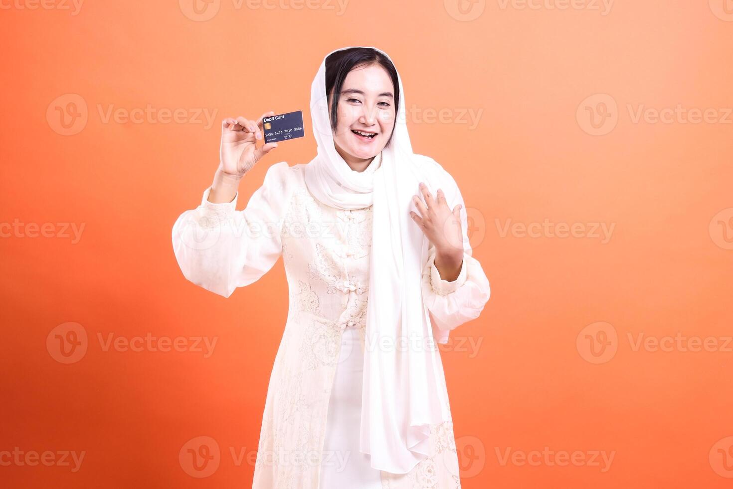 Happy Muslim Woman Holding a Credit Card Financial Empowerment, Banking Concept, and Modern Lifestyle, isolated on a orange background. photo