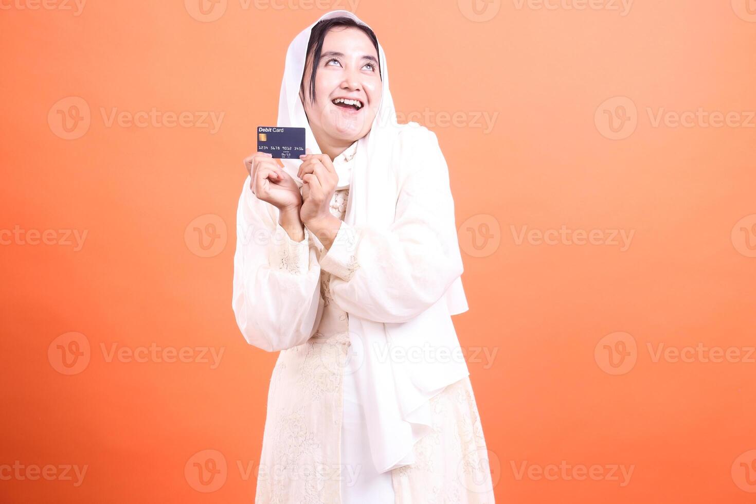 Happy Muslim Woman with Debit Card A Vision of Financial Freedom and Modernity in Islamic Finance, isolated on a orange background. photo