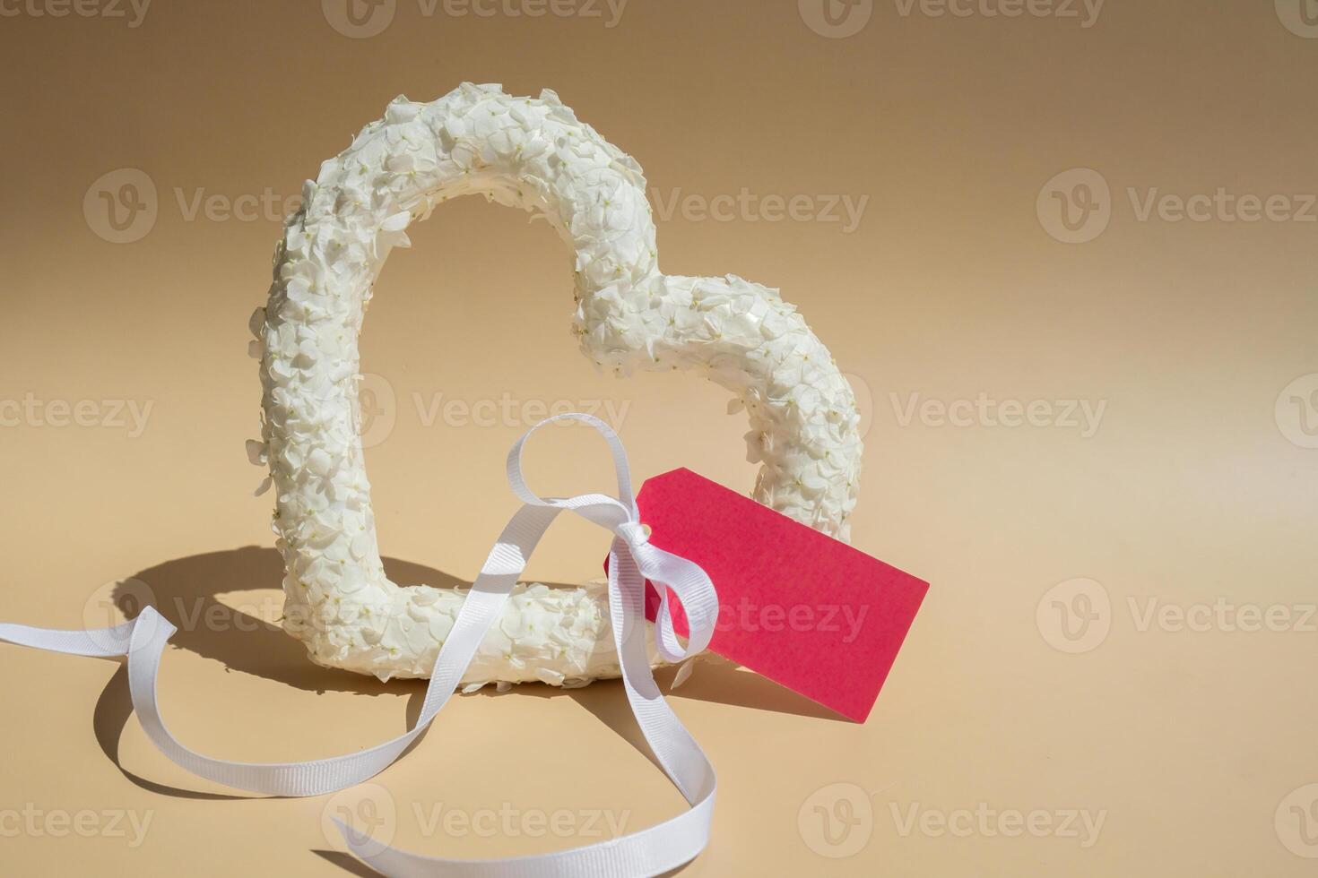 Heart made of white lilac flowers with pink mock up paper template on pastel beige background. Still life romantic composition of Valentines day holiday copy space for your text invitation greeting card postcard. photo
