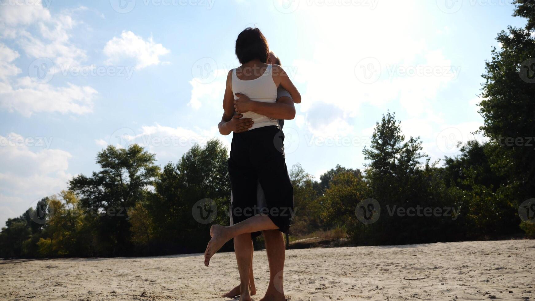 Happy couple spending time at sandy beach.Man kissing his beloved on seashore at sunny day. Carefree lovers resting during summer travel at coastline. Concept of vacation or holiday. Slow motion photo