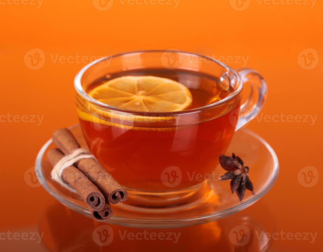 A cup of tea with lemon and cinnamon on an orange background photo