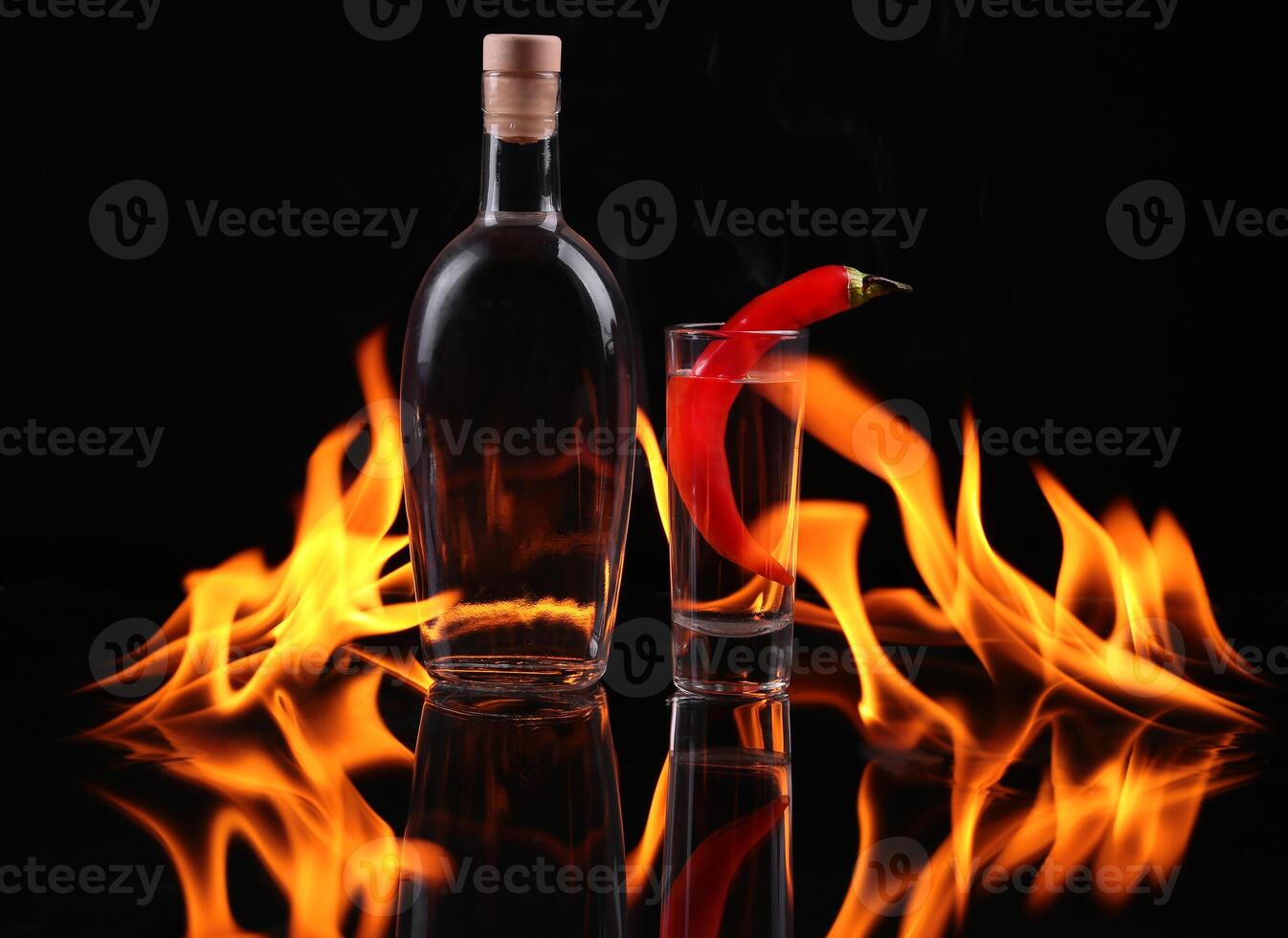 A bottle of vodka and a glass with a red pepper on fire photo