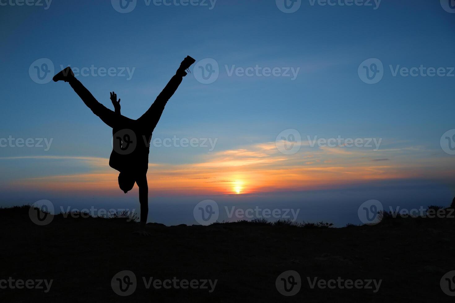 A person doing a handstand on top of a hill at sunset photo