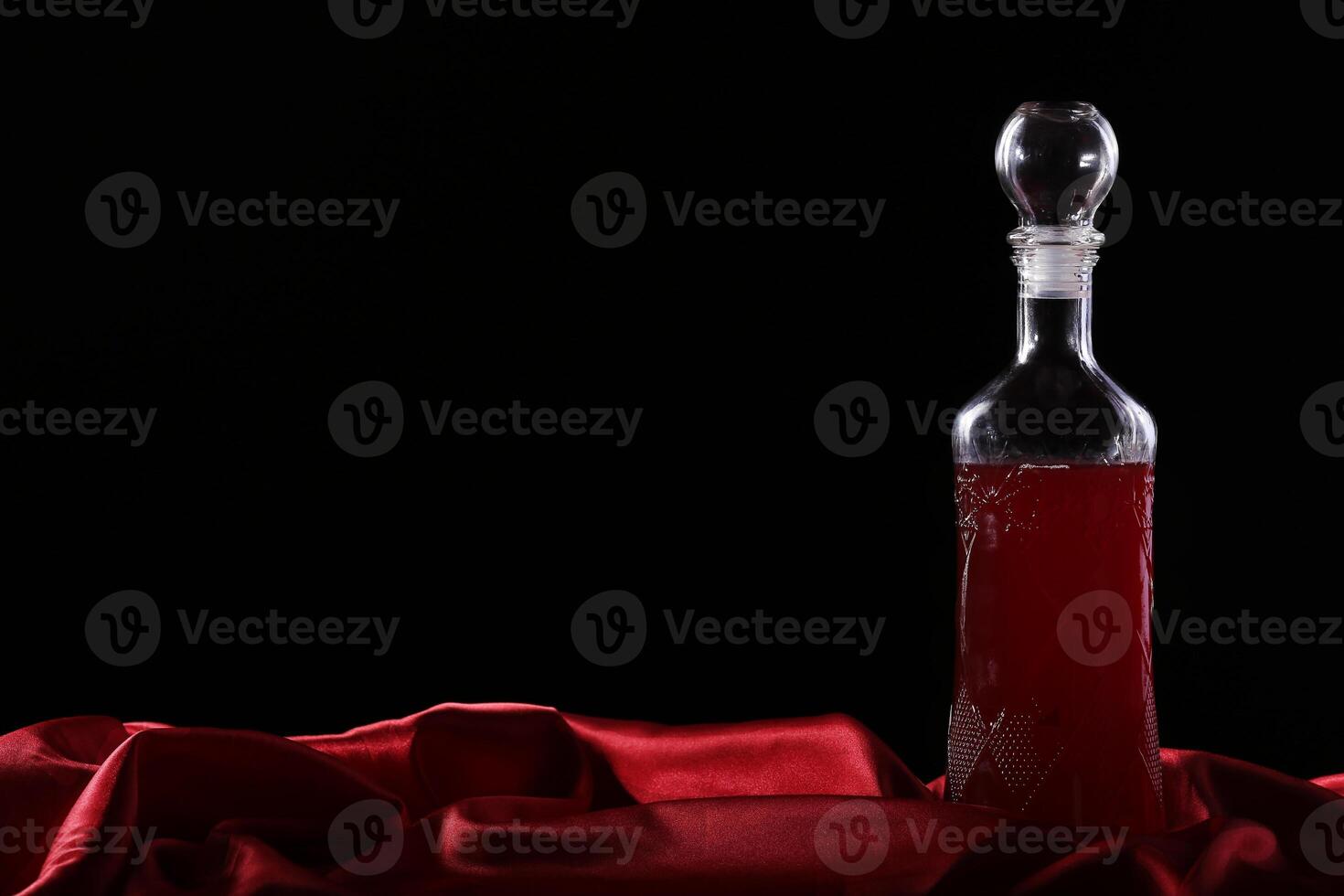 A bottle of red liquid sitting on a red cloth photo