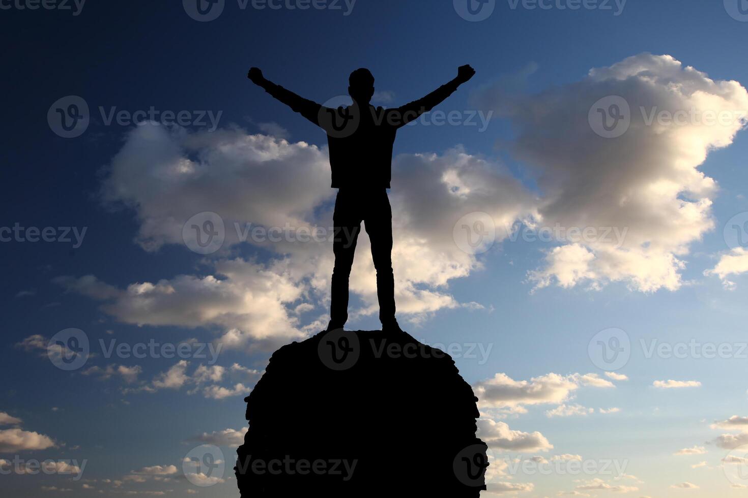 A man stands on top of a mountain with his arms raised photo