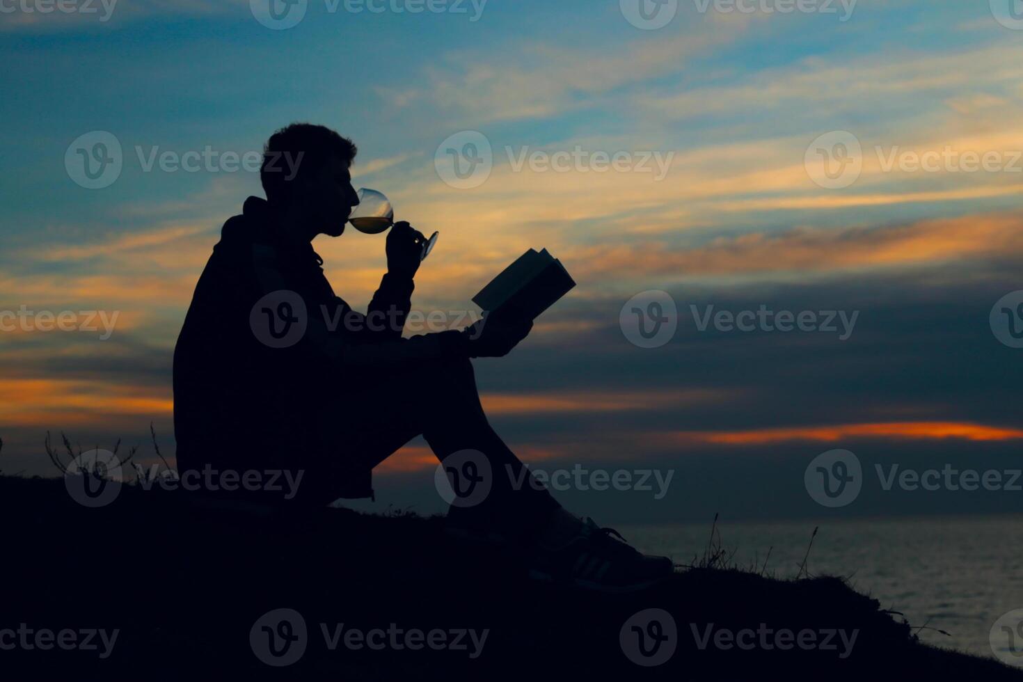 A man sitting on a hill with a book and a glass of wine photo