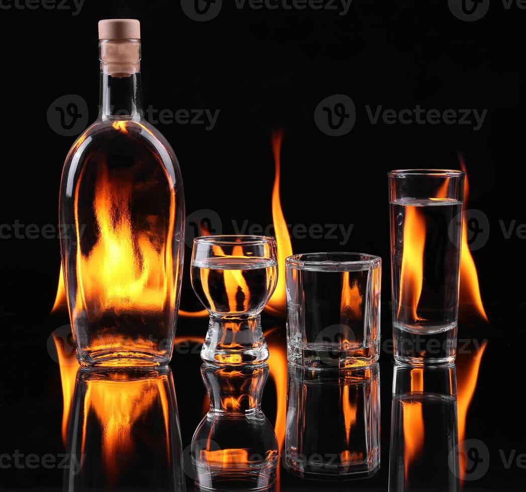A glass and a bottle of vodka are set on fire photo
