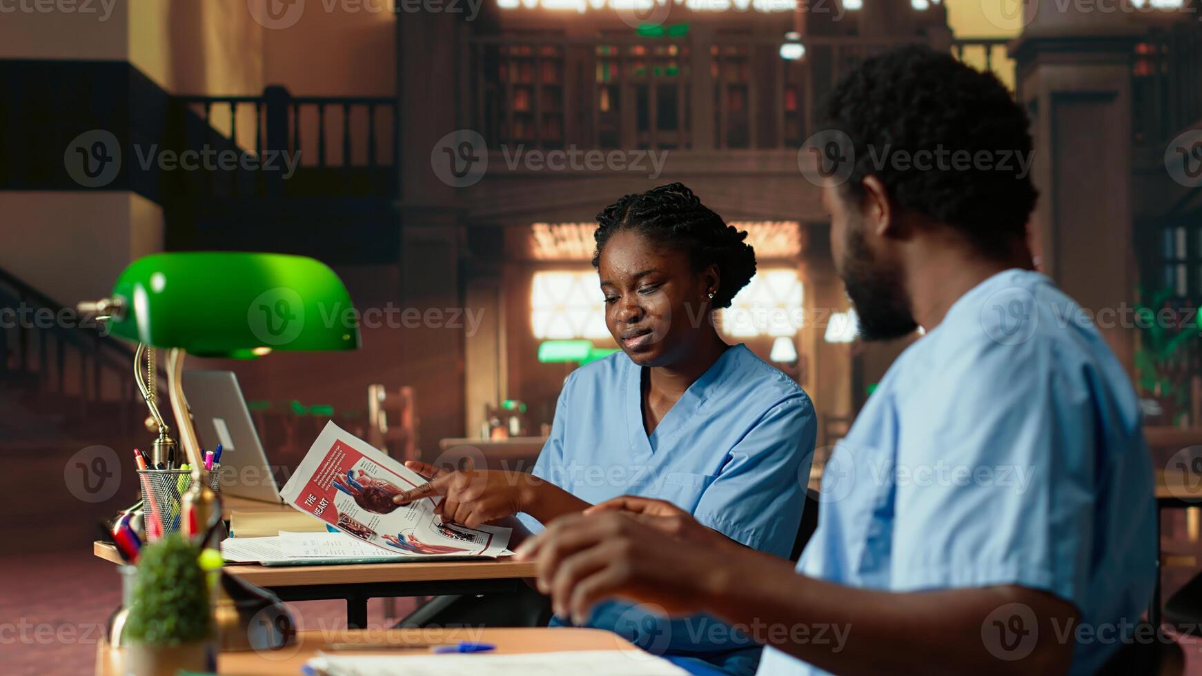 Nurses studying anatomy class notes in university library, reviewing courses and preparing for exams. Black med school students working together for medical education. Camera B. photo