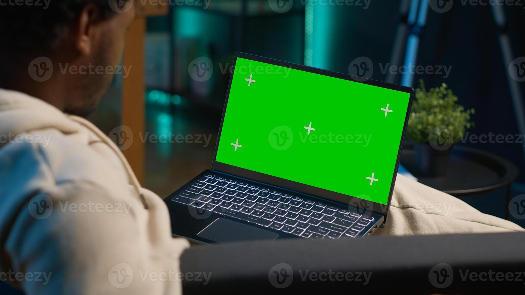 African american person using device with green screen from comfort of modern trendy home, sitting on couch and working in living room. Happy confident young man. Camera A. photo