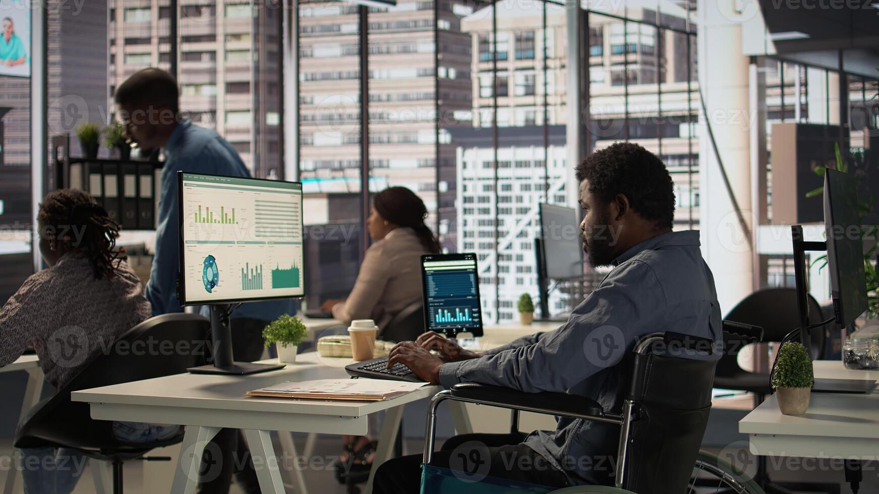 African american male worker in wheelchair trying to solve daily tasks at office, examining organizational data and working on forecasting plan. Man with impairment ensures analysis. Camera B. photo