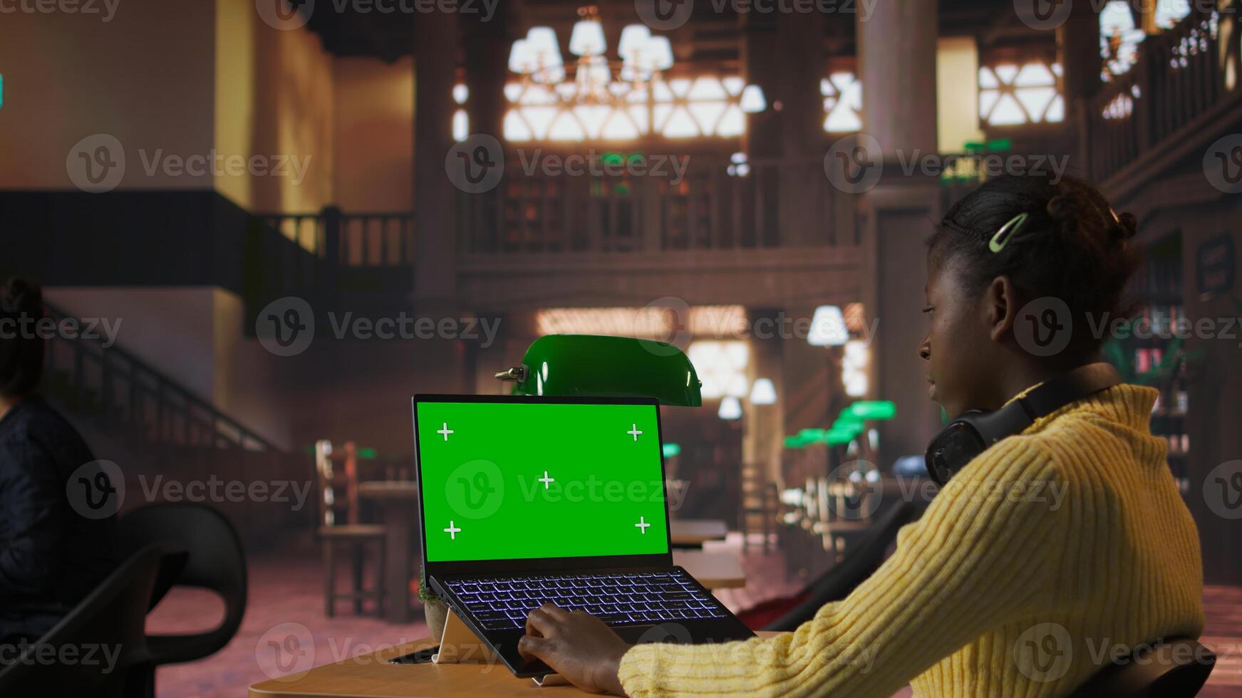 Black scholar reading information via internet next to chroma key in library, focusing on theoretical studies and completing class assignments. Taking notes for educational work. Camera A. photo