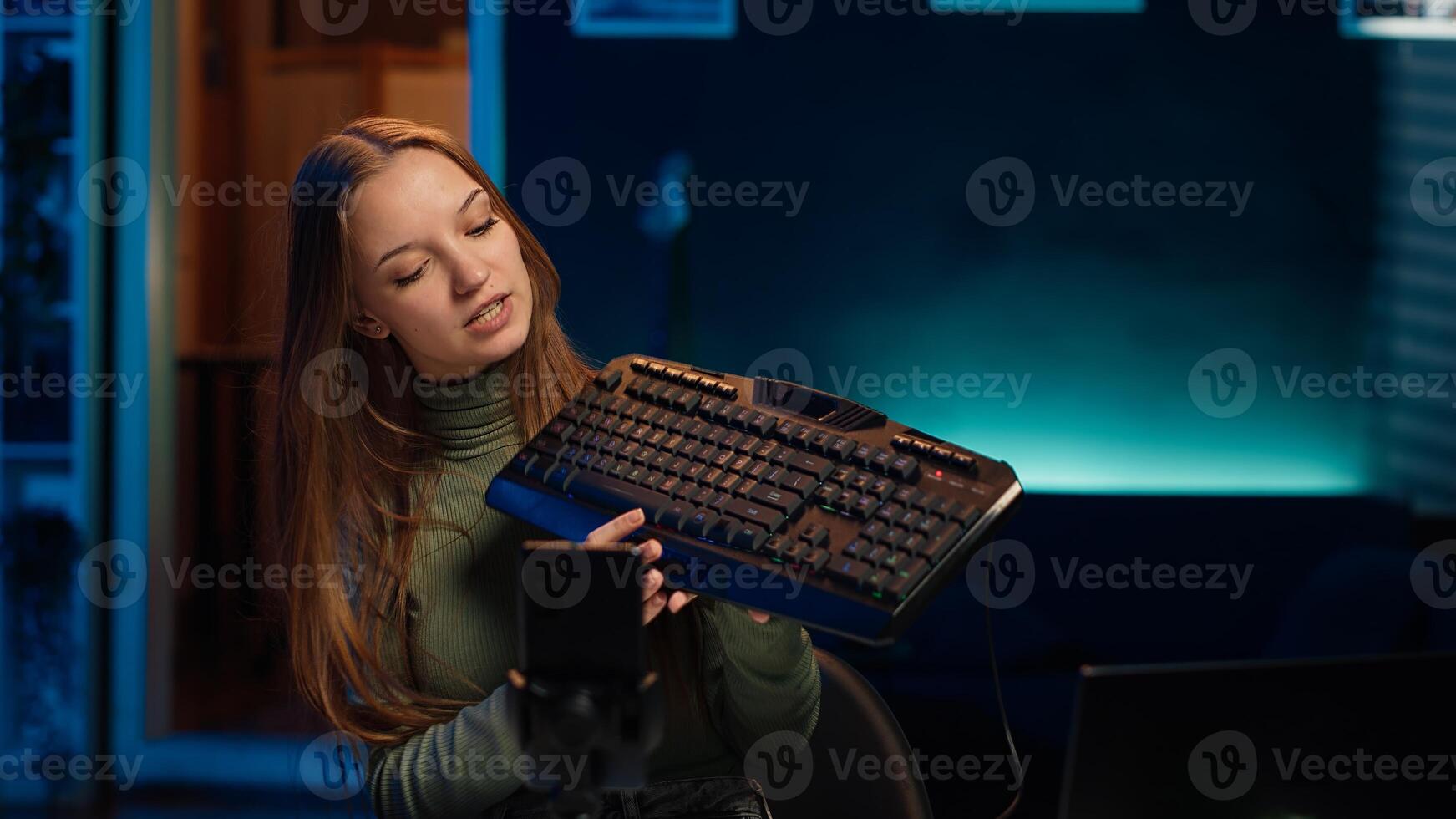 Gen Z girl presenting RGB lit mouse and keyboard, doing review in personal studio to see if price is justified. Young influencer showcasing neon lit computer peripheral features to fans, camera A photo