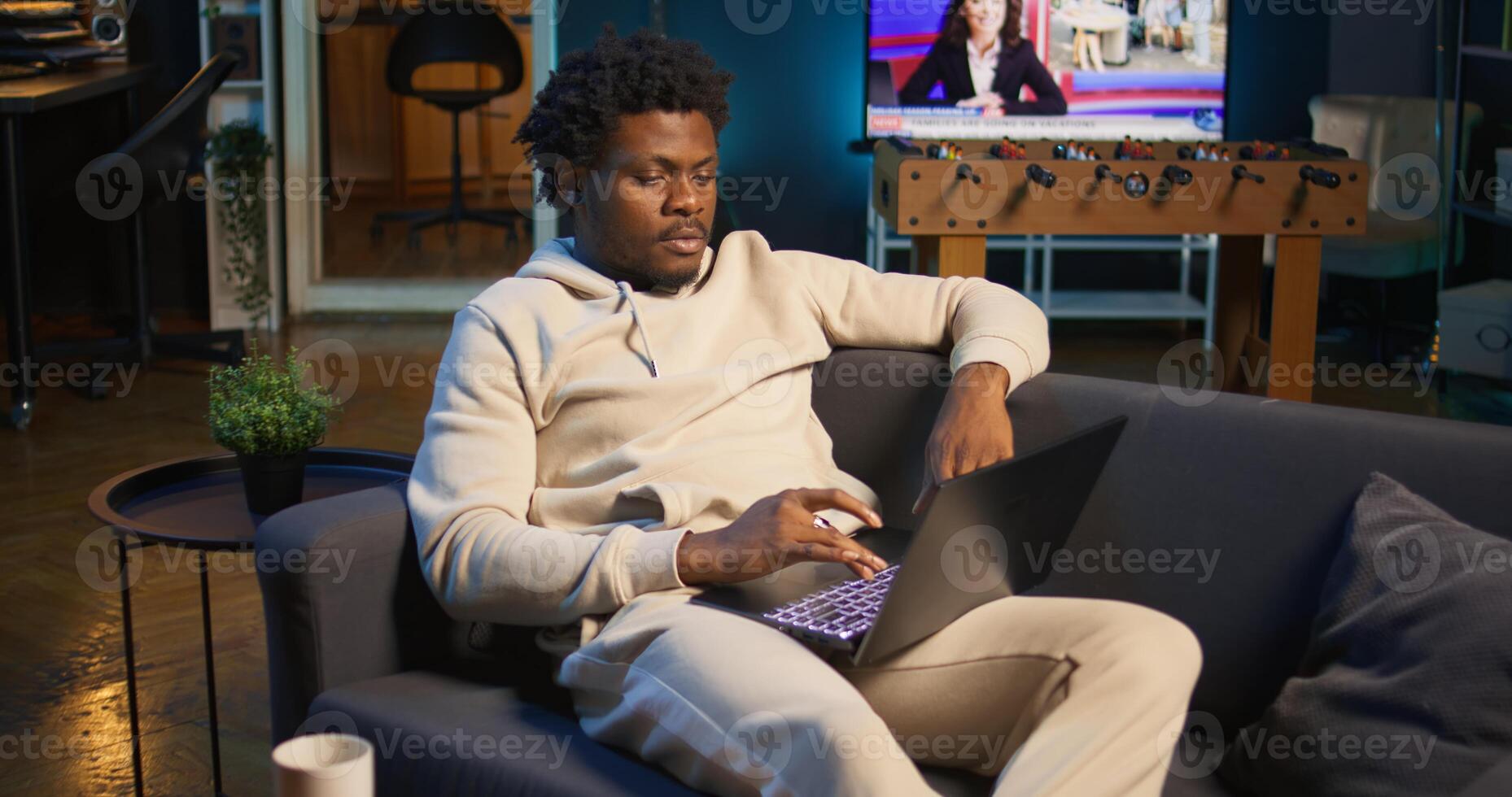 Adult man typing on laptop at stylish illuminated apartment, engaging in online work, multitasking efficiently and embracing flexibility of remote work in cozy home setting. Camera B. photo
