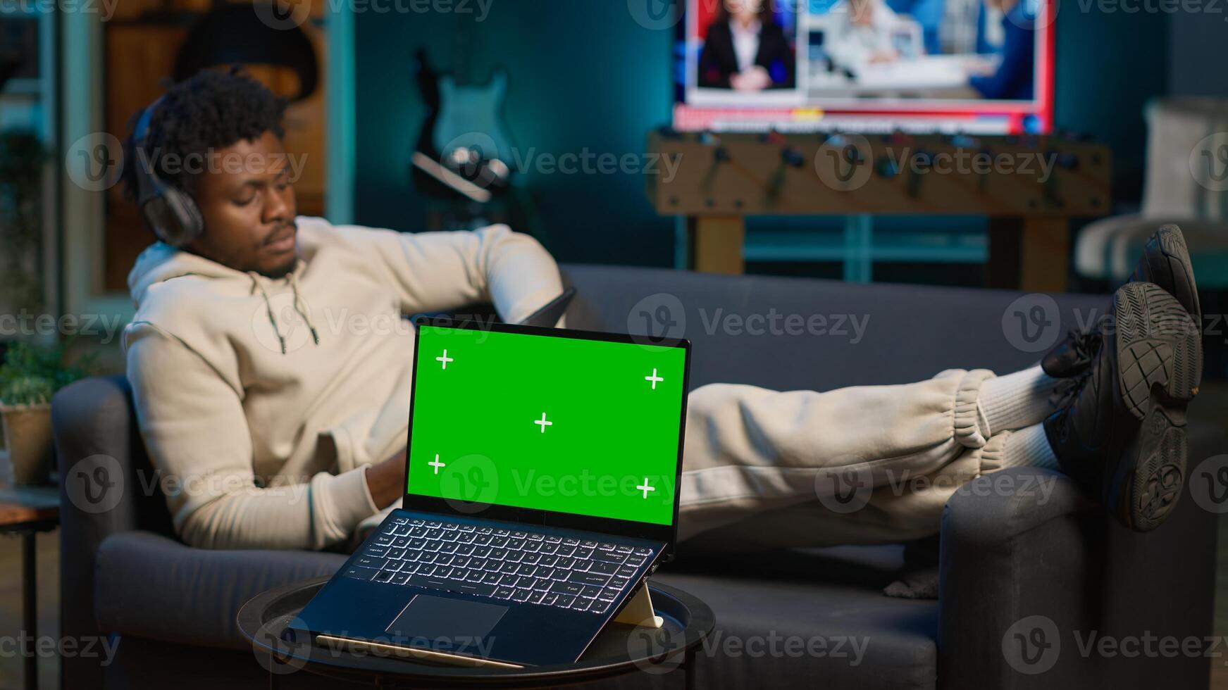 African american person enjoying music on headset next to copy space screen, feeling happy with remote work and relaxing on sofa. Relaxed chill guy sitting in trendy apartment. Camera A. photo