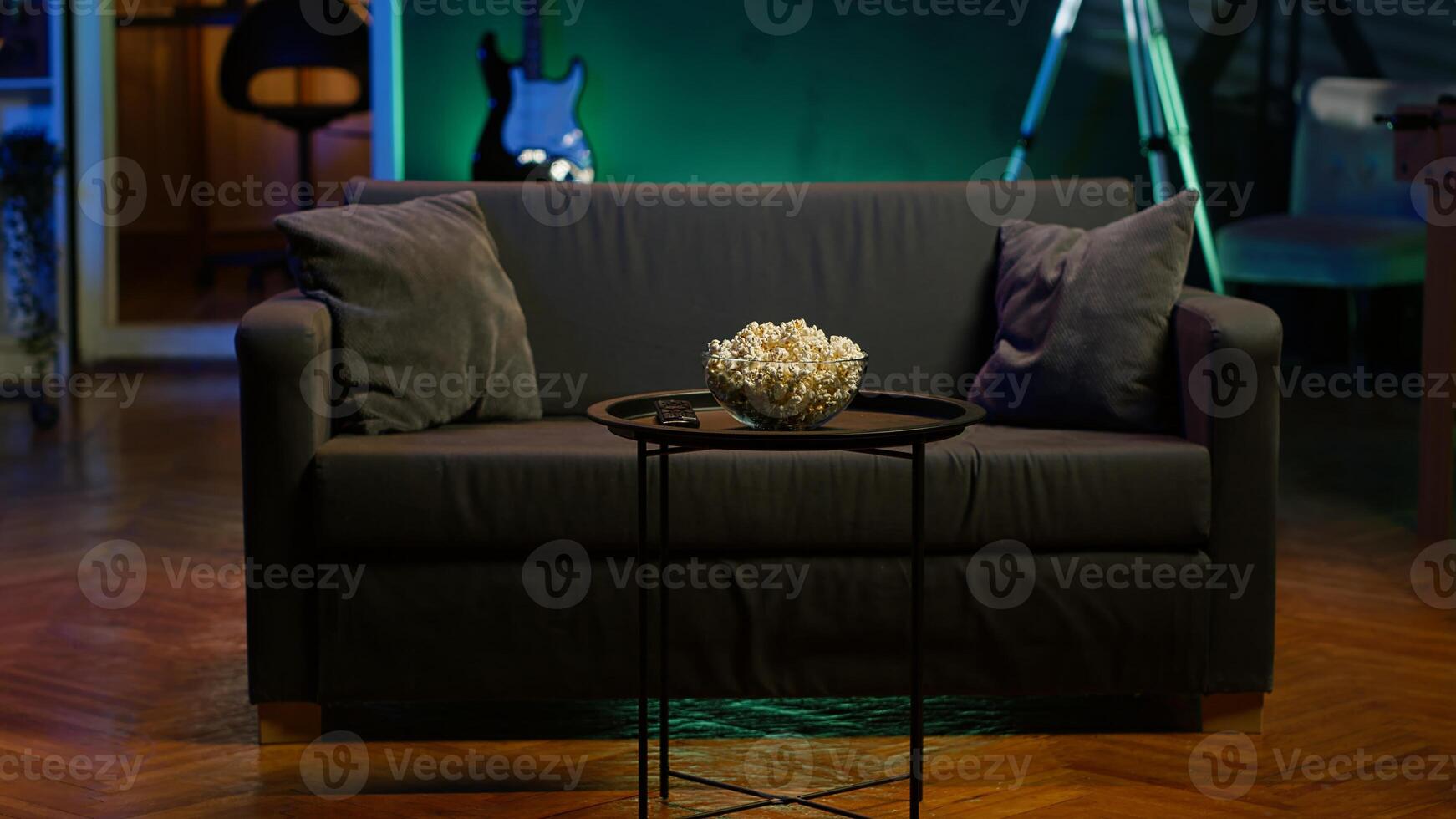 Cozy residential interior with sofa and snacks, ready for casual movie night or immersive TV viewing experience. Bowl of popcorn on table in neon illuminated home theater apartment photo