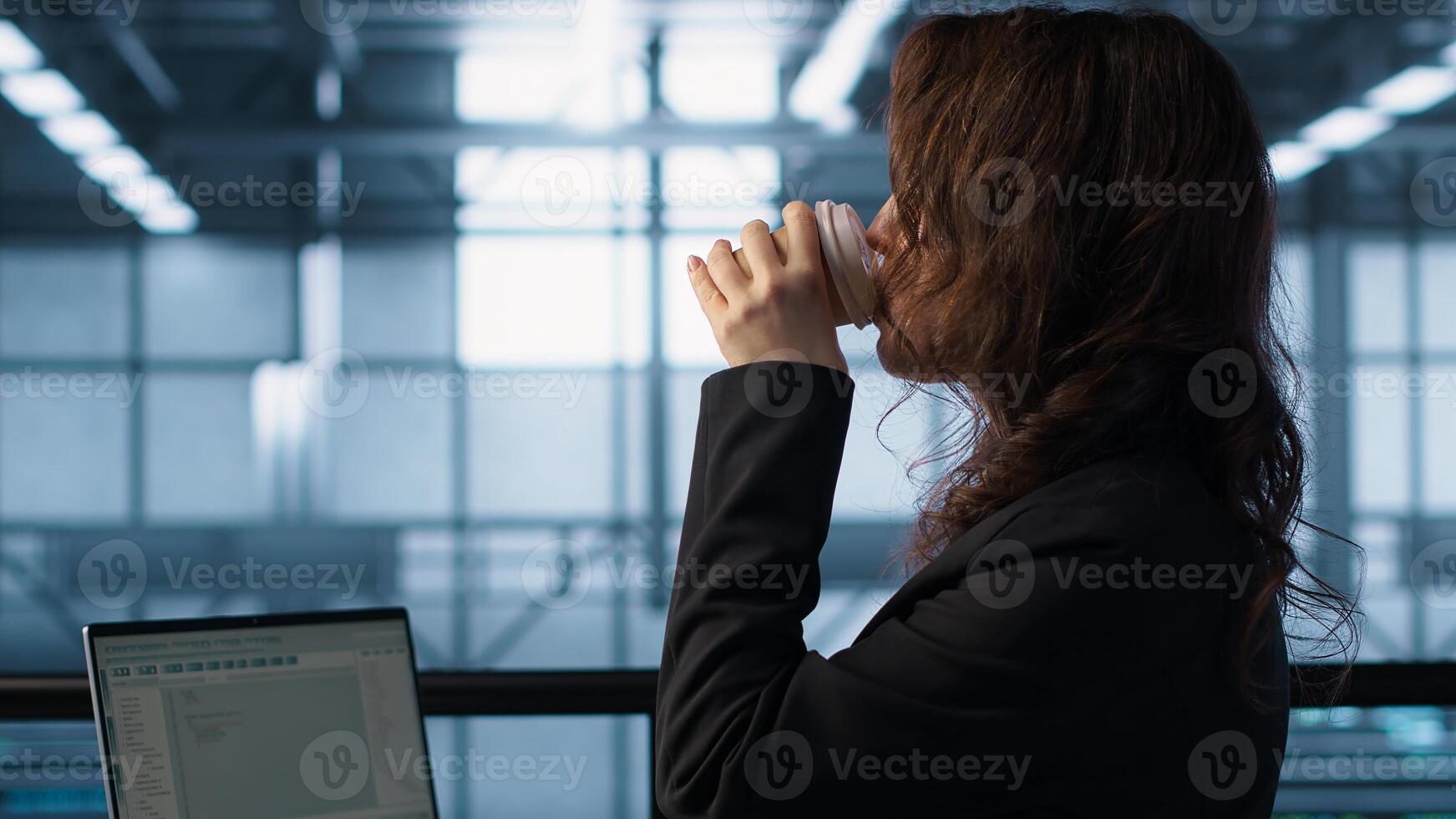 Technician using laptop in data center, finetuning network protocols and holding coffee cup. Woman in server room coding on notebook, enforcing advanced security measures, camera A photo