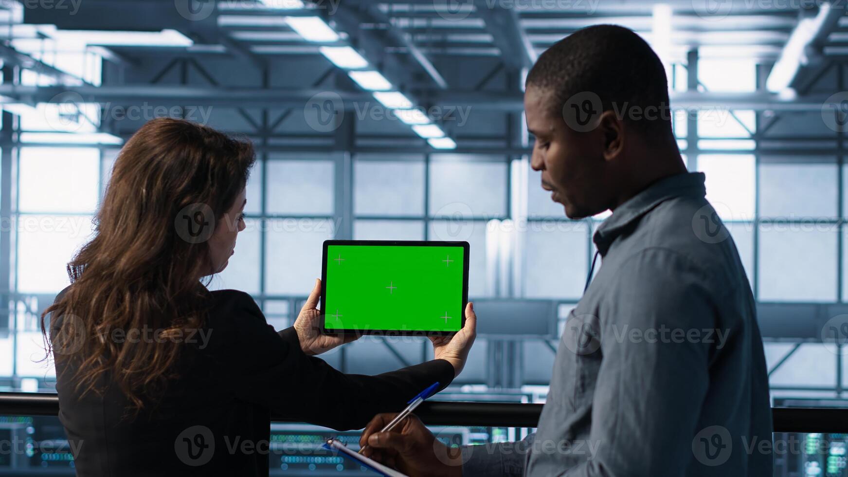 System administrators in server farm using isolated mockup tablet to verify settings. Data center colleagues using green screen chroma key device to monitor facility, camera A photo
