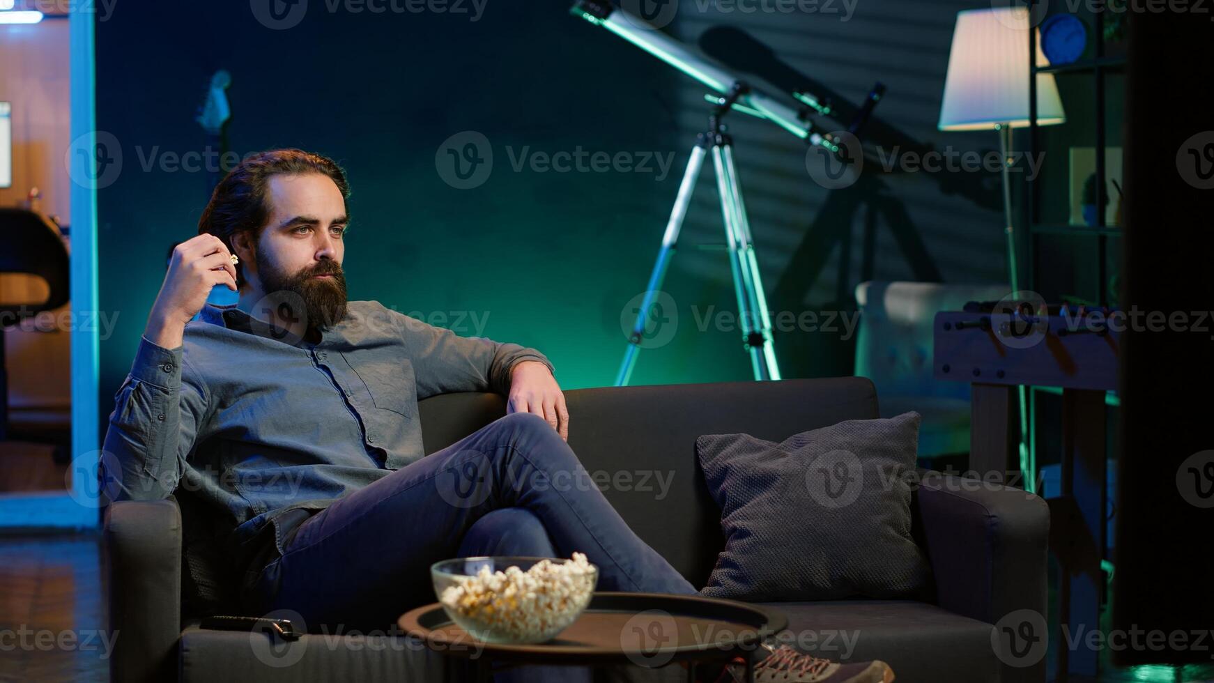 Man at home watching interesting movie on streaming service, enjoying time off from work. Person on couch enjoying high quality film on TV in apartment, camera A photo