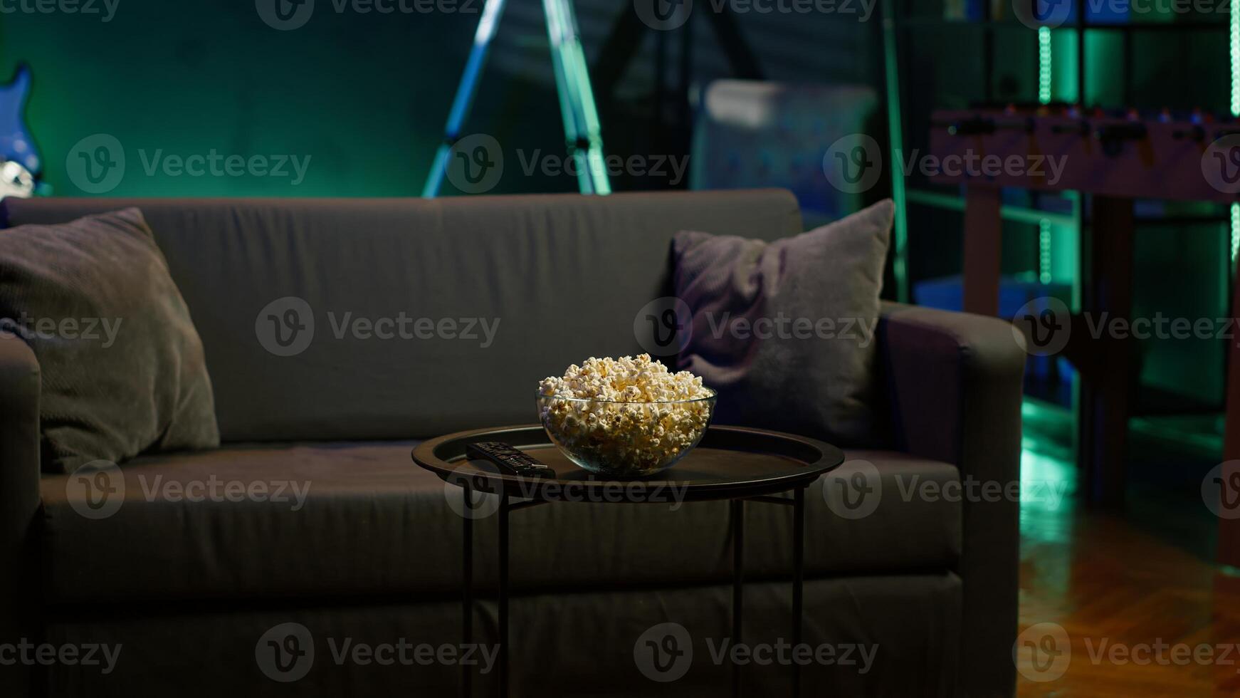 Snack prepared for movie night in dimly illuminated home theatre. Empty neon lit cozy residential interior with sofa and bowl of popcorn on coffee table. photo