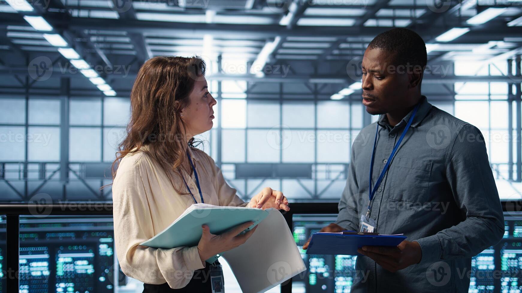 Cheerful admins meeting in data center to review reports and files, doing handshake. Server room employee saluting colleague, troubleshooting to prevent downtime, camera B photo