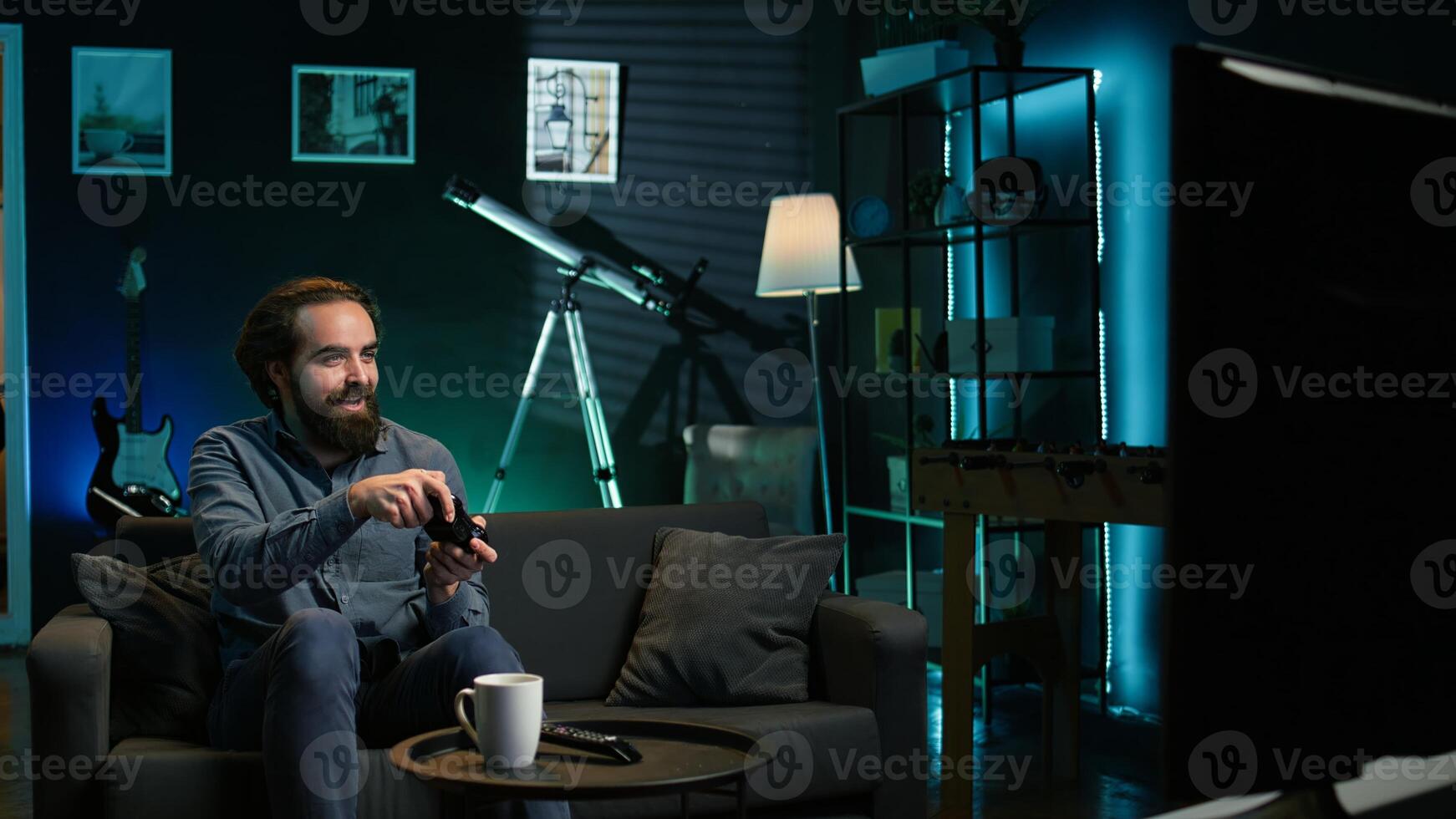 Man playing videogame in neon illuminated home, holding controller. Gamer excited to participate in online tournament, battling other players using professional joypad photo