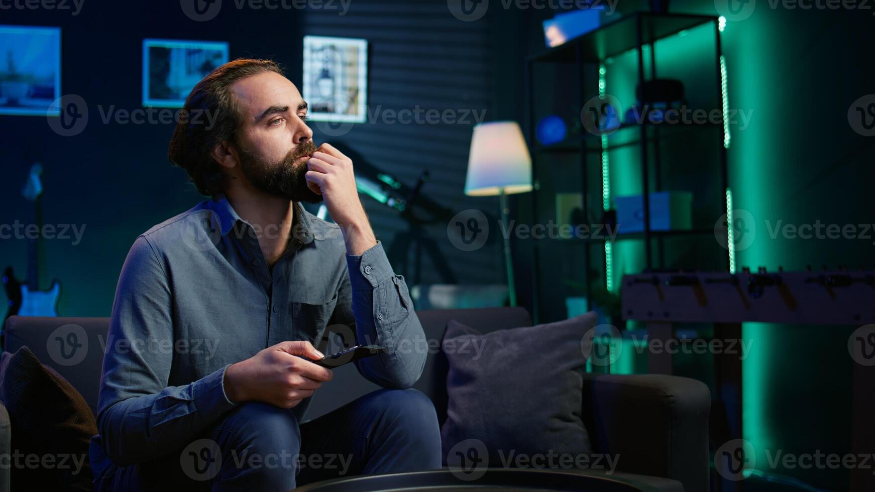 Bored man at home searching for series to binge on streaming services, procrastinating. Close up of person sitting on couch, flipping through TV channels using remote control, camera B photo