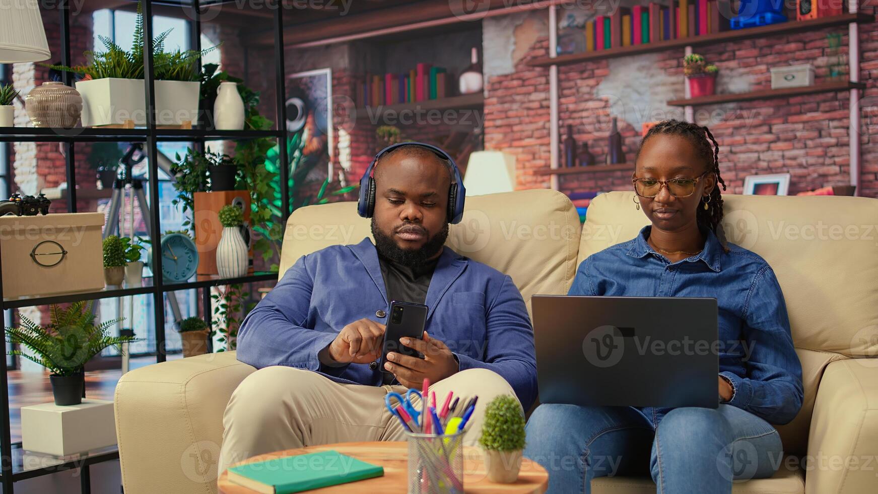 Woman working on freelance tasks while partner browses cellphone, modern couple using devices sitting on couch in living room. People enjoying time at home. Camera A. photo