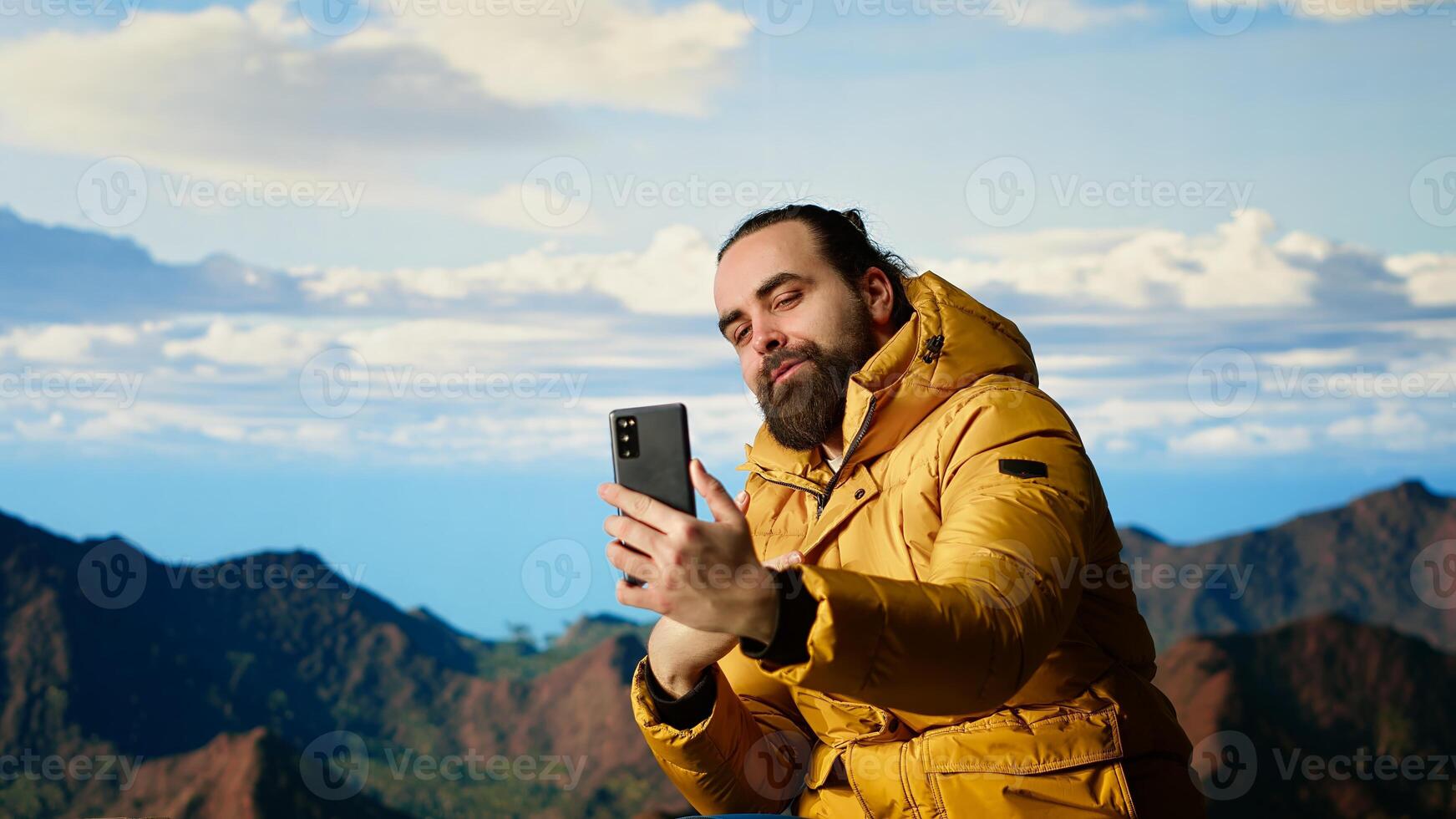 Determined adventurer enjoys panoramic mountain landscape, taking selfies with amazing scenic background on hill top where nature and towering peaks create breathtaking view. Camera B. photo