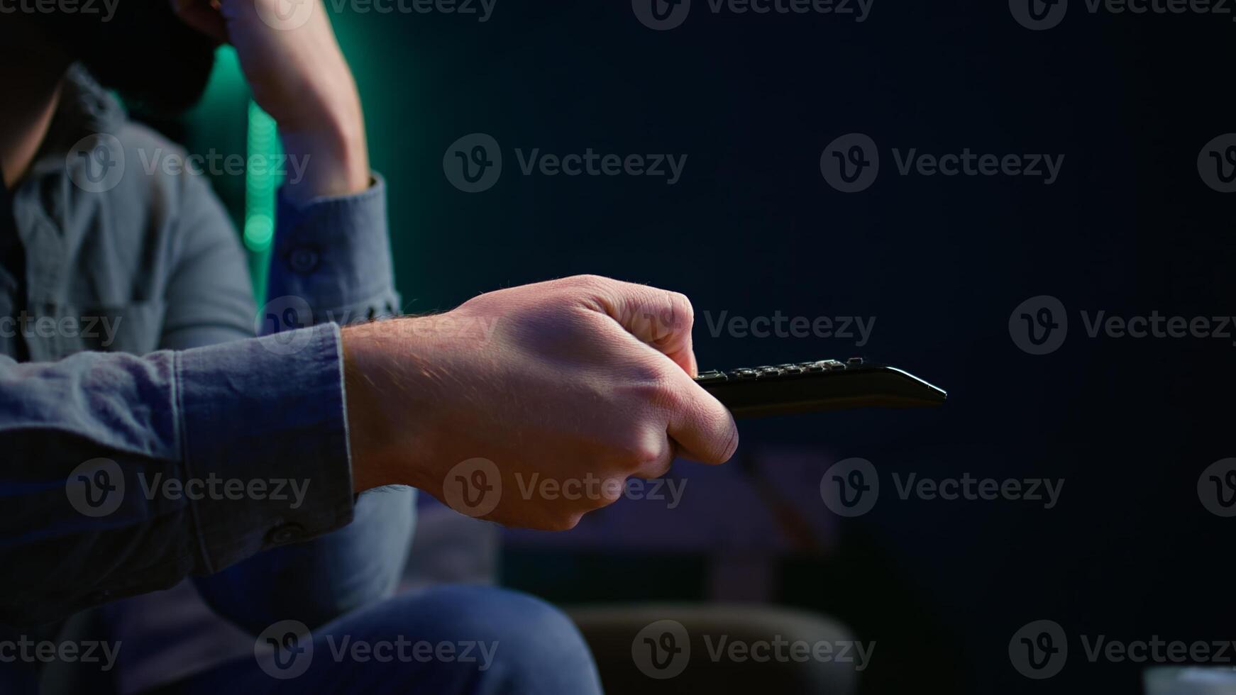 Close up of man on couch browsing through movies available on streaming service. Focus on remote control used by homeowner in apartment switching channels on TV, camera B photo