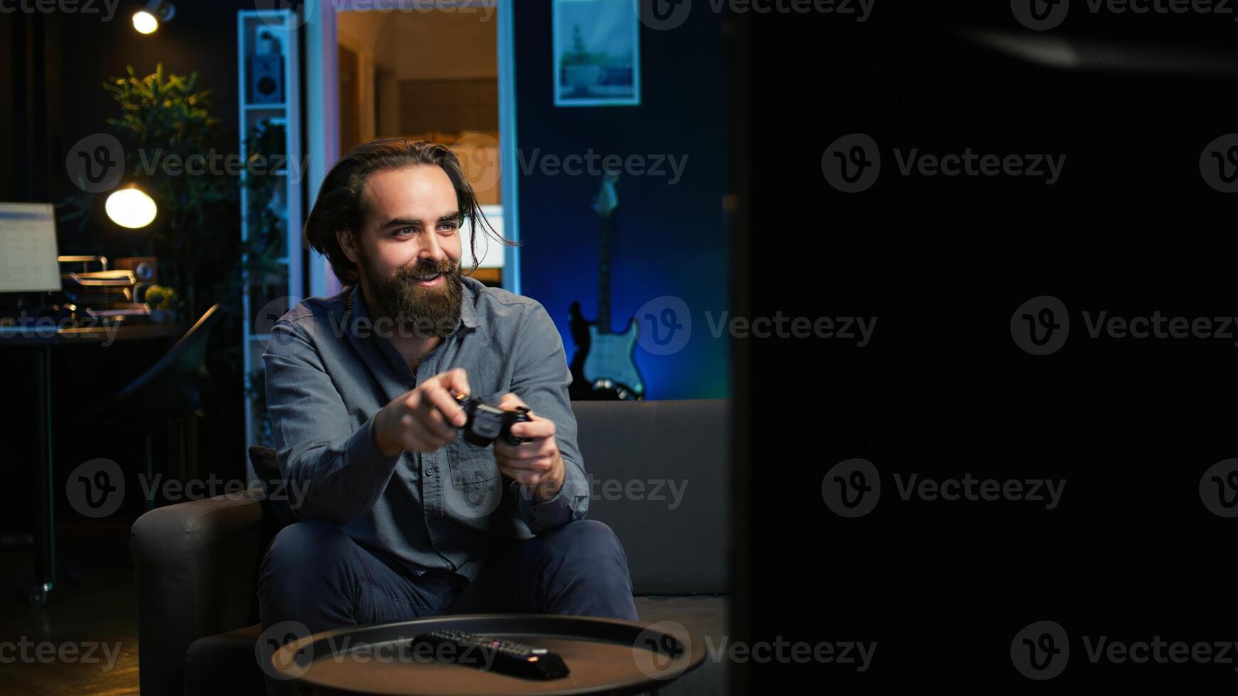 Cheerful gamer rushing home to play newly released game. Happy man jumping on couch, eagerly gaming on console, relaxing after hard day at work, camera B slow motion shot photo