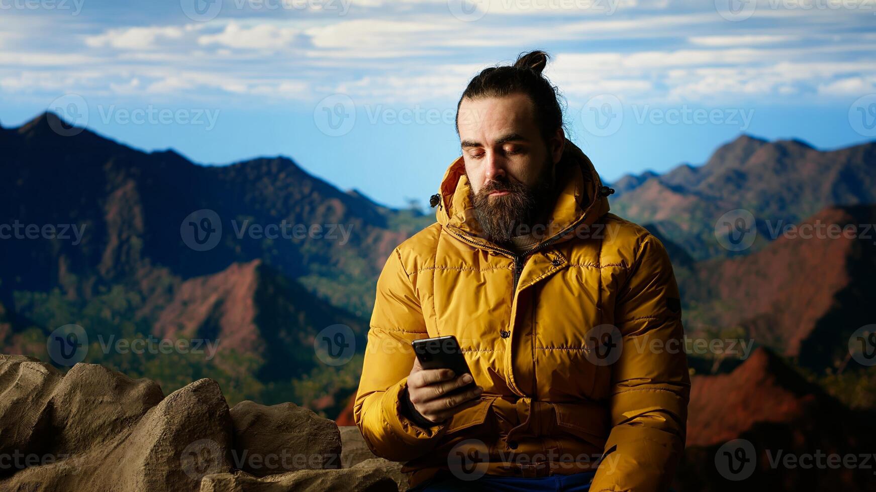 Nature lover relaxing on mountain top using phone at scenic viewpoint, looking out over landscape. Hiker staying always online and connected, panoramic scenery. Camera B. photo