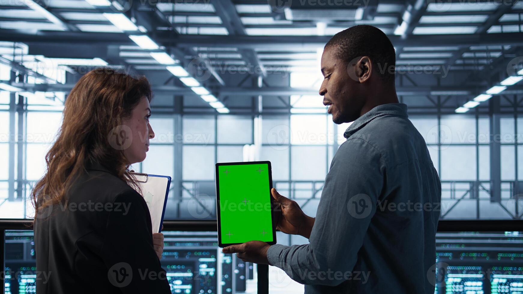 Data scientists using mockup tablet, conducting security audits to prevent bugs. African american man with colleague in data center looking at green screen device, camera B photo