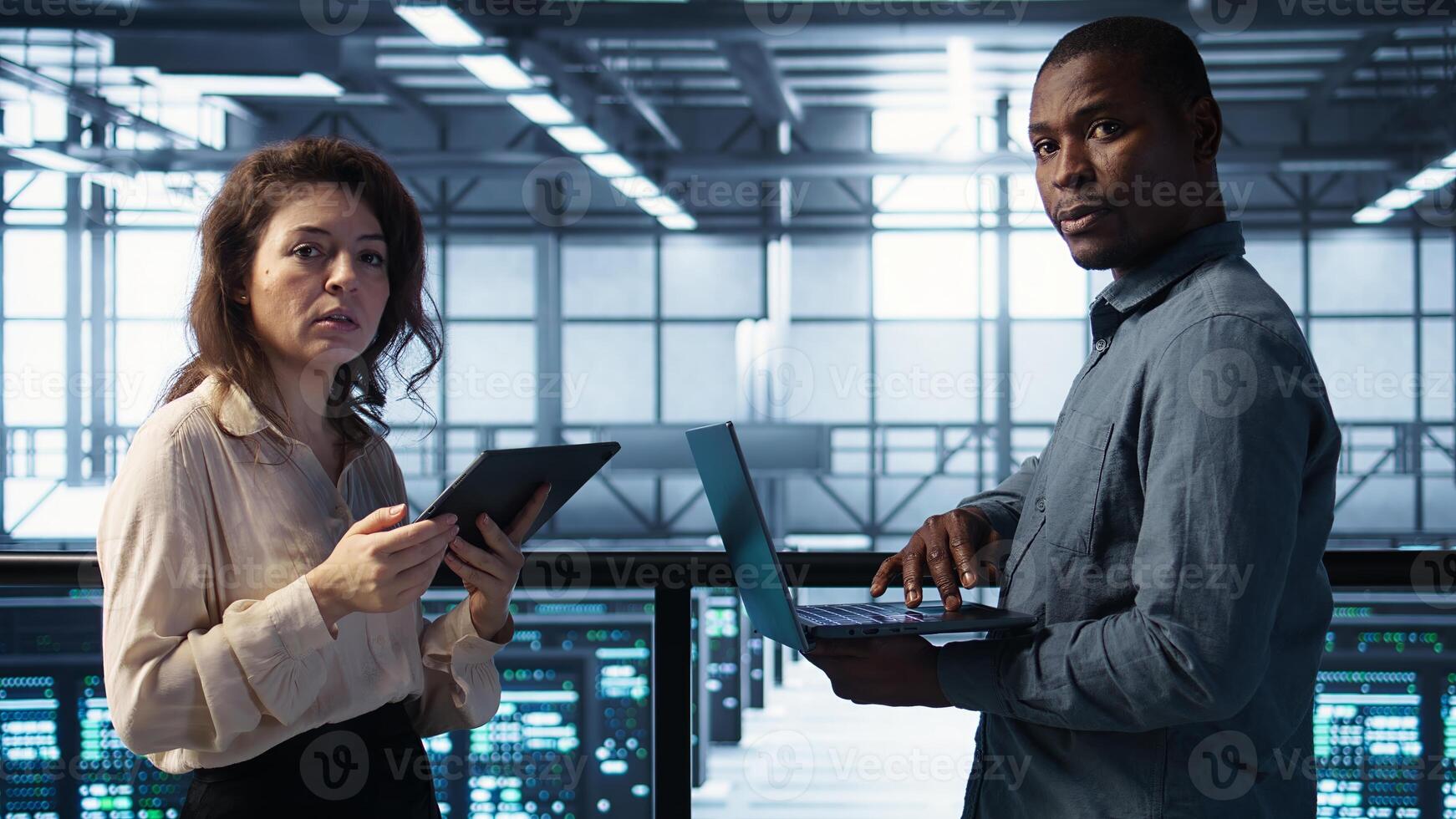 Scientists in server room using laptop and tablet, executing security patches and verifying firewall configurations. People performing equipment vulnerability scans in data center, camera B photo