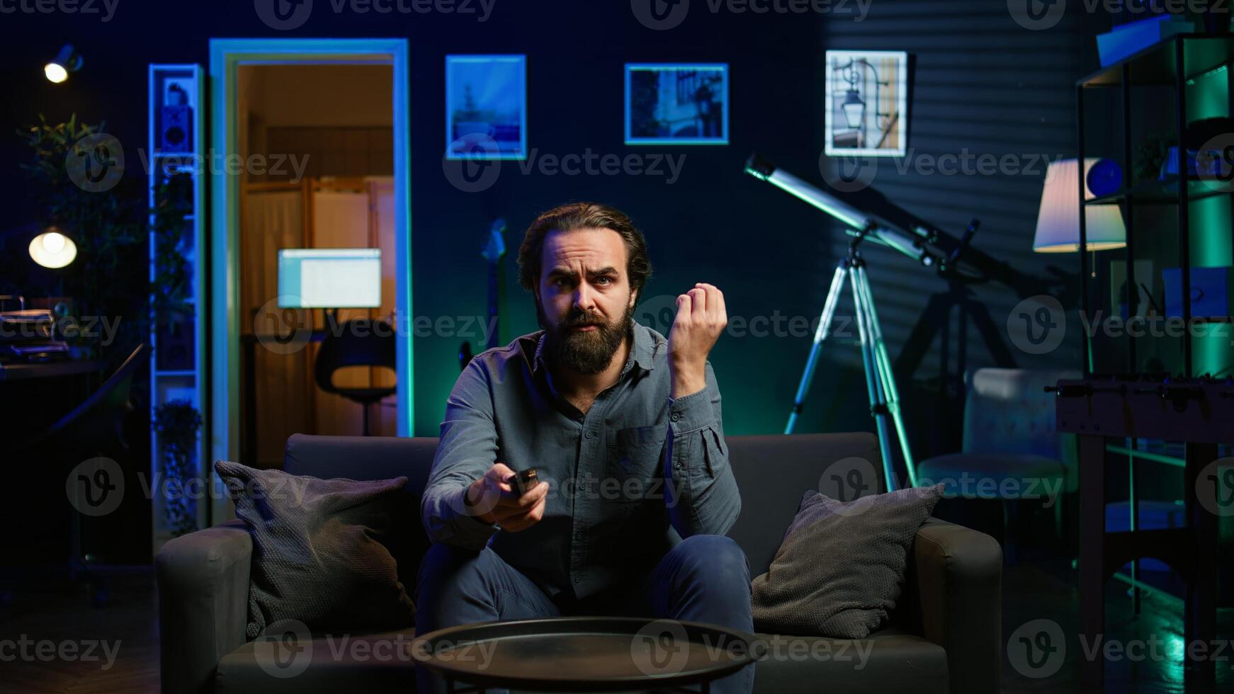 Frowning man watching sports on TV, flabbergasted by surprising goal conceded by favorite team. Appalled supporter looking at football match, reacting to player missing penalty, camera B photo