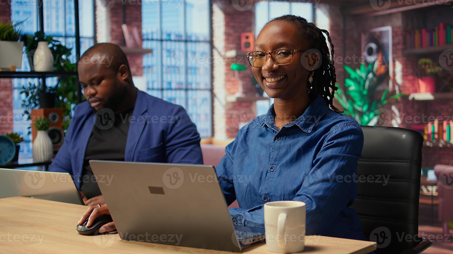 African american woman checking reports in notebook to solve tasks with partner, doing freelance work from comfort of home. Focused people doing research with laptop. Camera A. photo