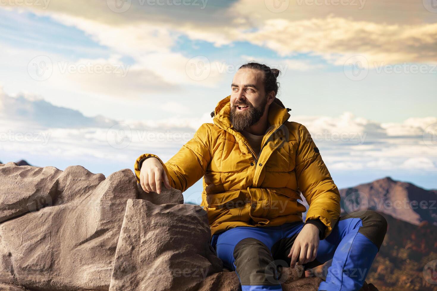 Traveler stands alone at edge of towering mountain range, gazing at clouds and stunning panoramic scenery. Pleased hiker showcasing personal growth and perseverance. photo