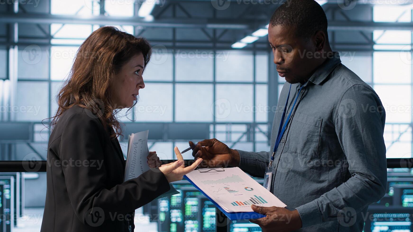 Data center team examining paperwork files and reviewing system diagnostics. Server room workers looking over maintenance schedules and cybersecurity protocols, camera A photo