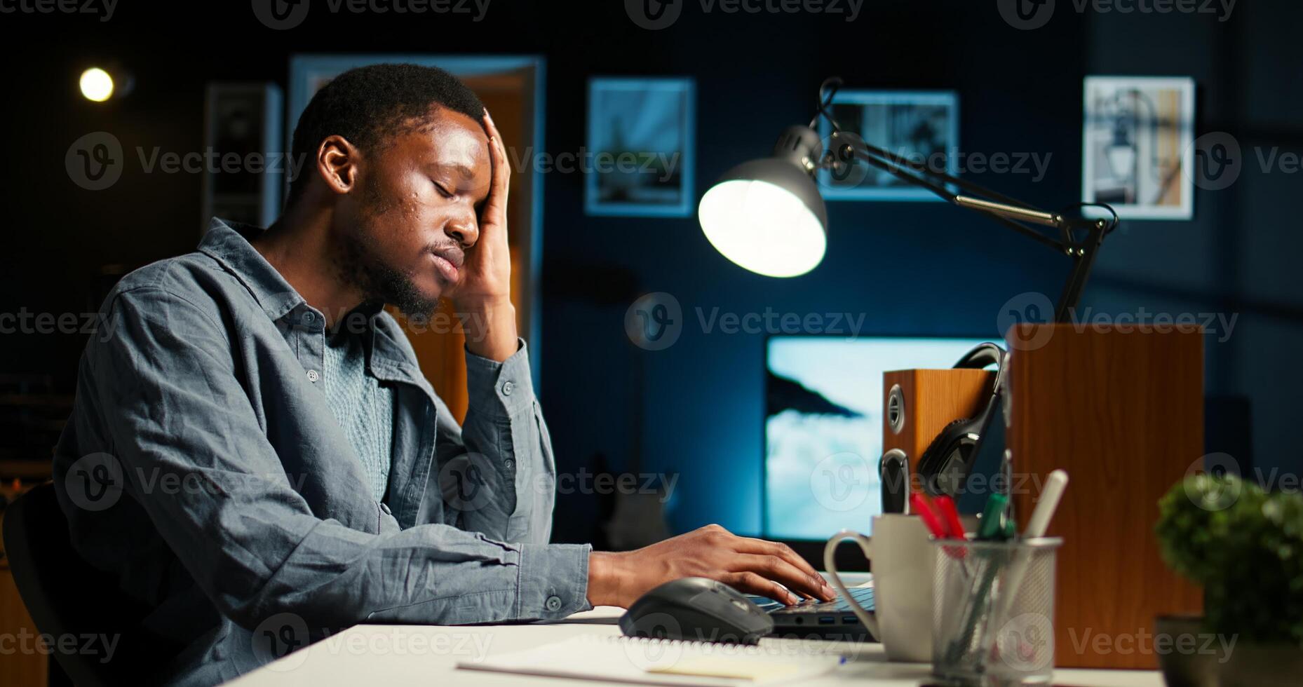 Self employed man feeling fatigued and stressed at home desk, trying to focus on solving tasks and dealing with tension of meeting deadlines. Young adult working on new contract. Camera A. photo