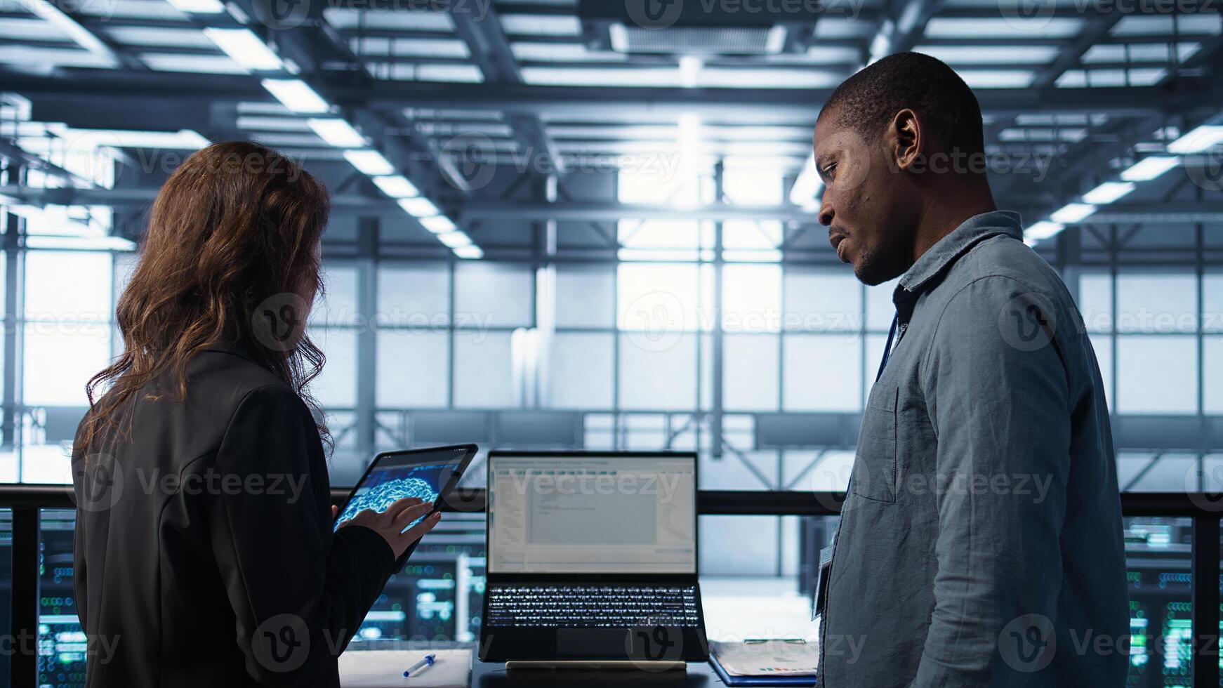 Programmers using AI technology on laptop and tablet in data center employing machine learning models. Devices used by artificial intelligence experts in server farm, camera B photo